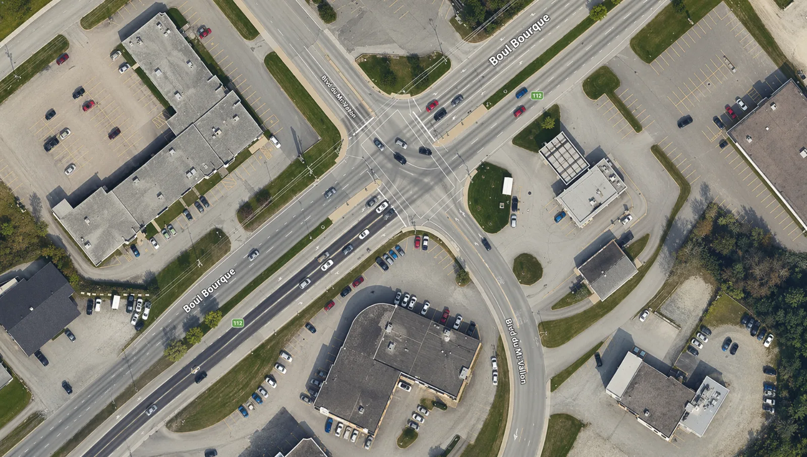 Vue aérienne de l'intersection du boulevard Bourque et du boulevard du Mi-Vallon, à Rock Forest : la route 112, multi-voies, bordée de commerces et de stationnements.